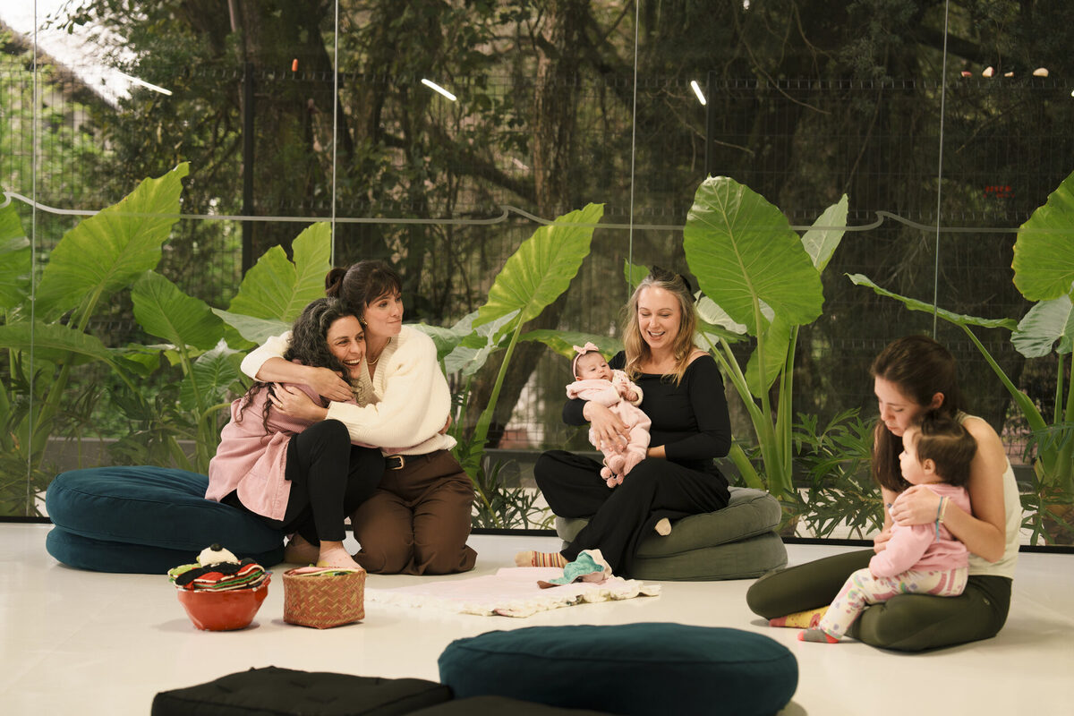 Grupo de mães se abraçando e sorrindo, com bebês no colo, durante um encontro do Parental Lab