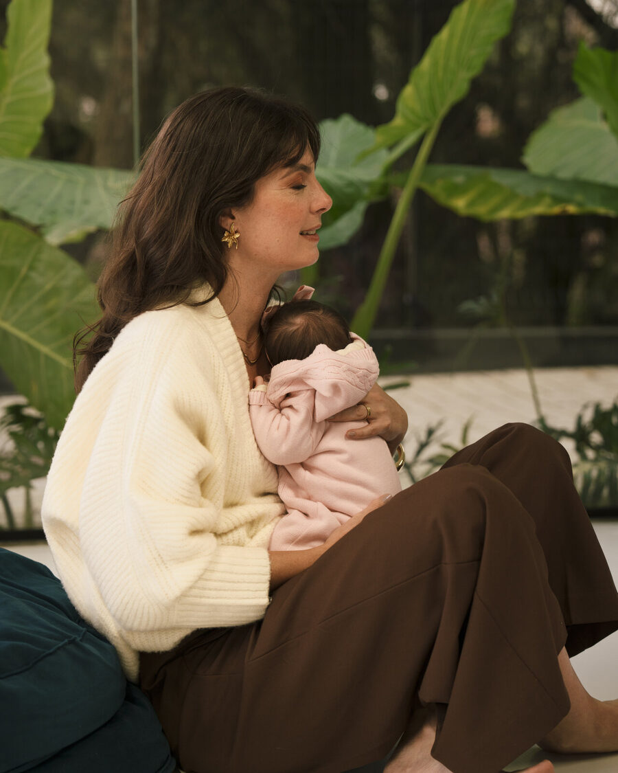 Luciana Lima acolhendo um bebê no colo, em ambiente cercado de folhagem