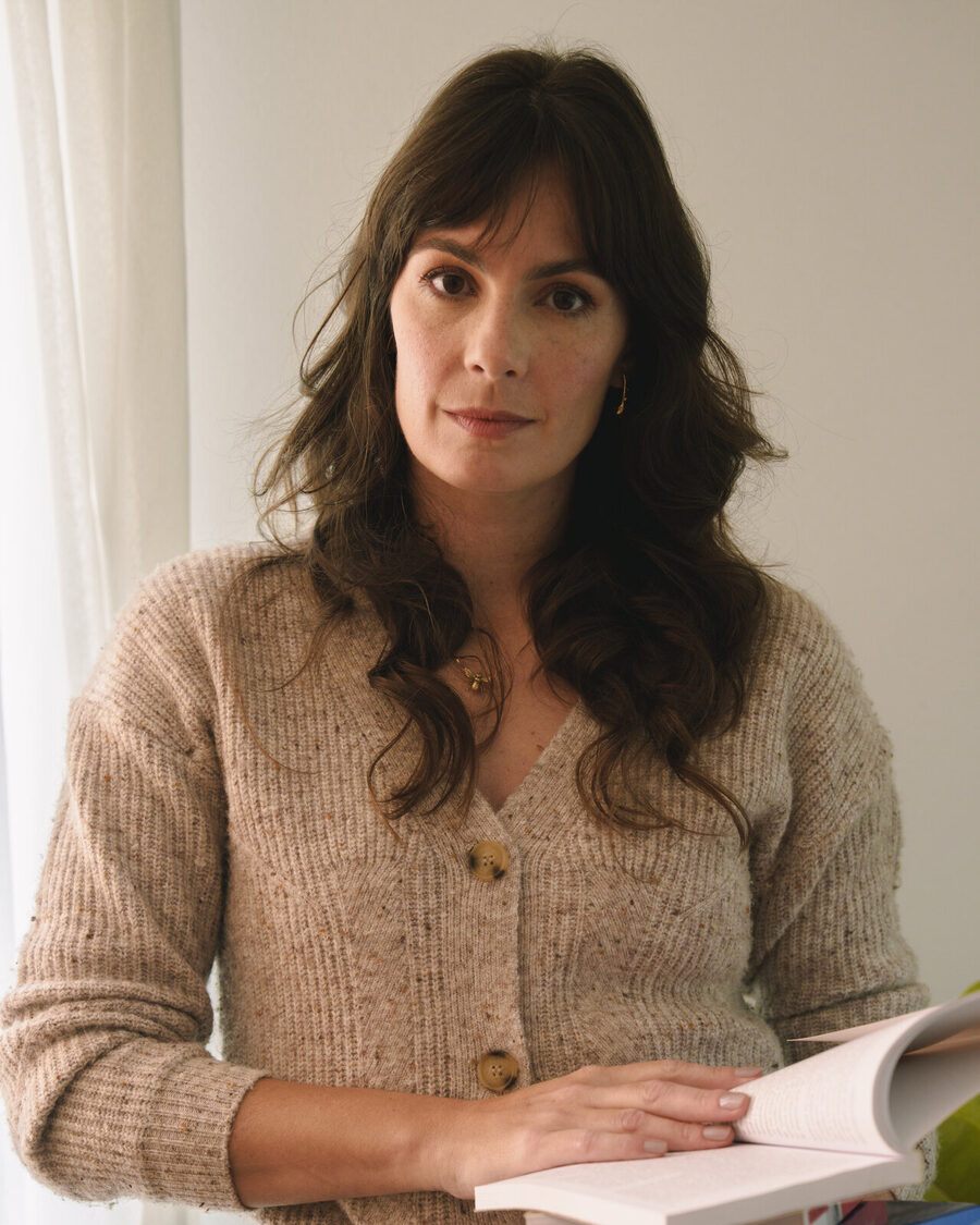 Luciana Lima segurando um livro, em retrato com suéter bege