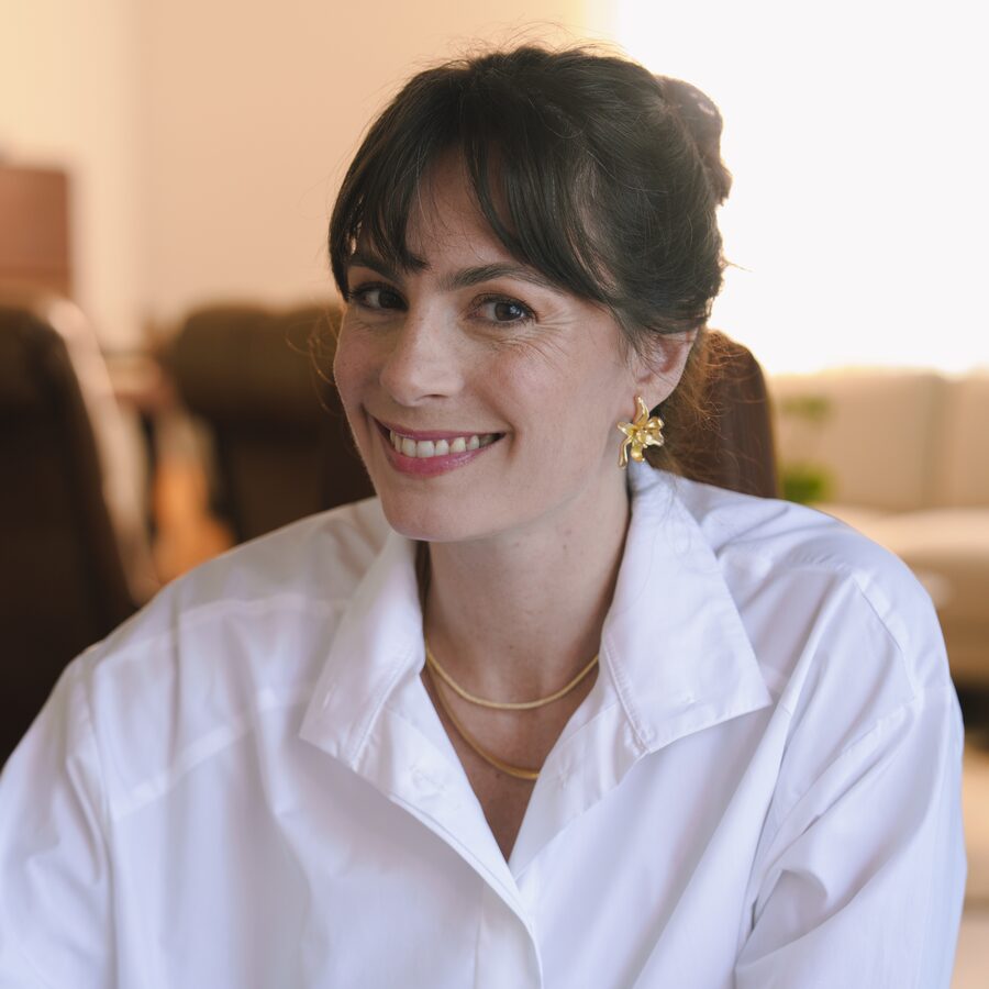 Luciana Lima, psicóloga, sorrindo sentada à mesa, usando camisa branca